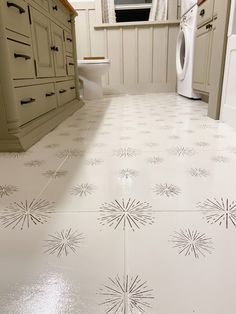 a kitchen floor with white tile and starburst designs on the floor, in front of a washer and dryer