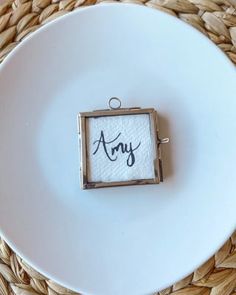 a white plate topped with a small square frame on top of a wooden table next to a woven place mat