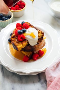 a white plate topped with french toast covered in berries and syrup being drizzled over it