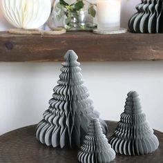 three paper christmas trees sitting on top of a wooden table next to a candle holder