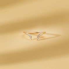 a gold ring with two small diamonds on the front and side, sitting on a beige background