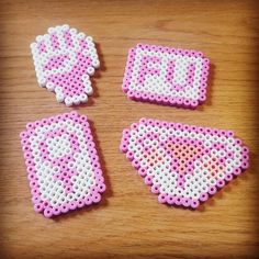 three pieces of pink and white perler bead art on a wooden table top