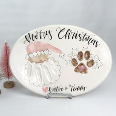 a white platter with dog paw prints and merry christmas written on the side, next to a pink tree