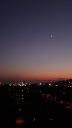 the moon is seen in the sky over some buildings and trees at night with lights on