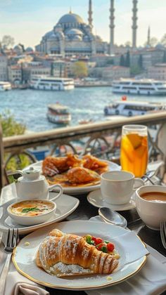 a table topped with plates of food and cups of coffee next to a body of water