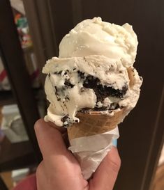 someone holding an ice cream cone with chocolate chip cookies and oreo cookie on top