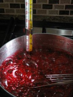 red liquid being stirred in a pan with a thermometer next to it on a stove