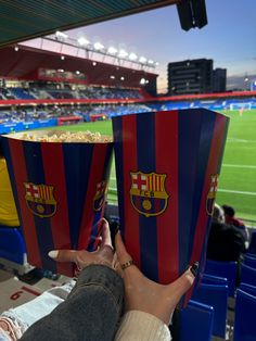 two people are holding up red and blue striped popcorn boxes in front of a stadium