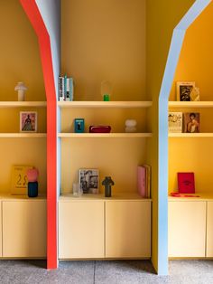 two shelves with books and pictures on them in a room that is painted yellow and orange