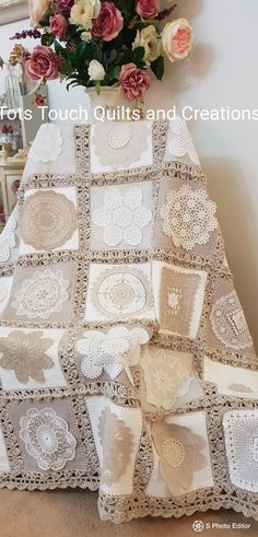 a white crocheted blanket sitting on top of a floor next to a vase with flowers