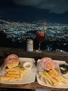 two plates with sandwiches and french fries on them in front of a cityscape