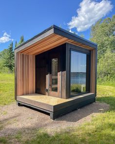 an outdoor sauna in the middle of a field with trees and water behind it