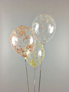 three clear balloons with gold sprinkles on sticks in front of a white wall