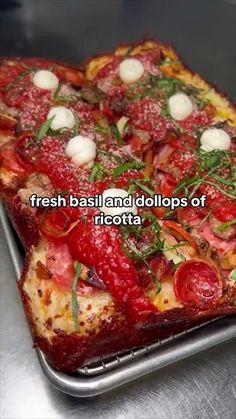 there is a square pizza with tomatoes and herbs on it's top, sitting on a metal tray