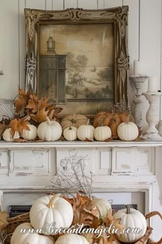 white pumpkins and gourds are arranged on a mantle in front of a painting