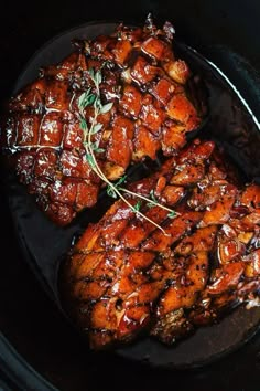 two pieces of meat in a slow cooker with herbs on the top and sauce on the bottom