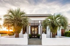 a white house with two palm trees in front of it and the sun going down