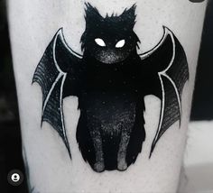 a black bat tattoo on the leg of a person's leg with white eyes