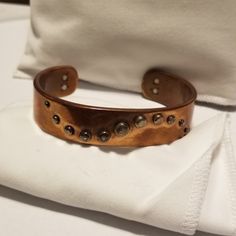 a brown leather bracelet sitting on top of a white cloth next to a white bag