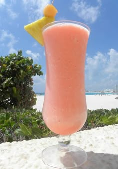 a pink drink sitting on top of a sandy beach