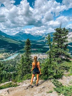 a woman standing on top of a mountain looking down at the valley and mountains in the distance