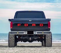 the rear end of a black ford truck parked on top of a sandy beach next to the ocean