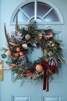 a wreath is hanging on the front door, decorated with autumn foliage and feathers for an elegant touch