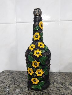 a bottle with sunflowers painted on it sitting on a counter top next to a tile wall