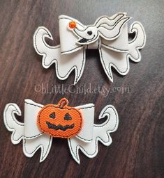 two white and orange halloween bows with pumpkins on them, sitting on top of a wooden table