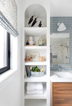 a white bathroom with shelves filled with towels and other items on the shelf next to the sink