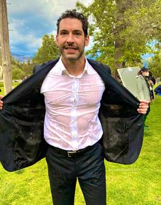 a man in white shirt and black pants holding up his jacket while standing on grass