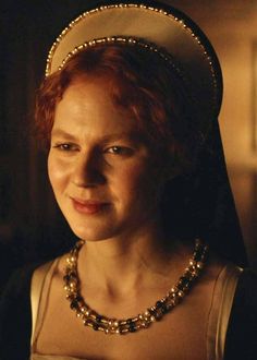 a woman with red hair wearing a white hat and gold beaded necklace in a dark room