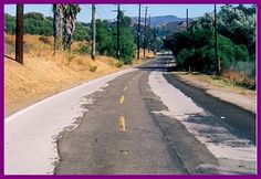 an empty road with trees and hills in the background