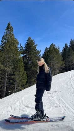 a woman riding skis on top of a snow covered slope with trees in the background