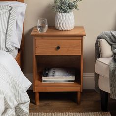 a nightstand with a wine glass on it next to a white chair and a bed