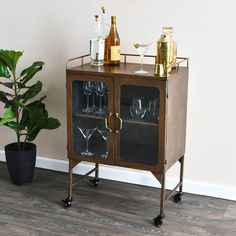 a wooden cabinet with wine glasses and bottles on it next to a potted plant