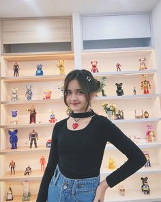 a woman standing in front of shelves with toy figures on it's sides and holding her hands on her hips