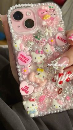 someone is holding their phone case with hello kitty and other things on it in her hand