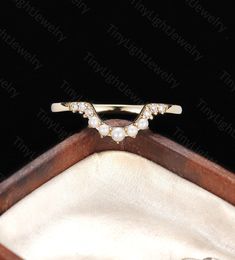 a gold ring with pearls and diamonds in it sitting on a wooden box next to a black background