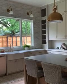 a kitchen with white cabinets and an island in front of two windows that look out onto the backyard