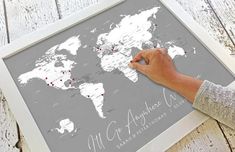 a person writing on a world map with pins in the middle and red dots all over it