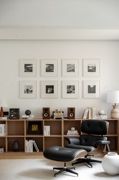 an eames chair and ottoman in front of a bookcase with many pictures on the wall