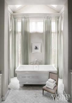 a white bath tub sitting in a bathroom next to a window with green drapes