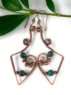 a pair of copper and green earrings hanging from a branch with leaves in the background