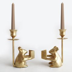 two gold colored candlesticks with one holding a book and the other holding a mouse