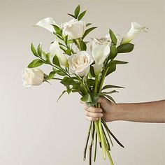 a person holding a bunch of white roses in their hand with greenery on the stems