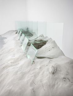 an artistic sculpture made out of glass sitting on top of a snow covered hill in front of a white wall