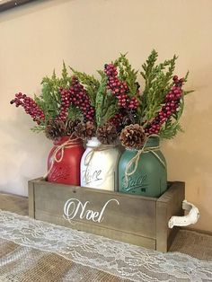 two mason jars with pine cones and berries are sitting on a wooden box that says noel