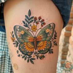 a butterfly tattoo on the side of a woman's thigh, with flowers and leaves around it