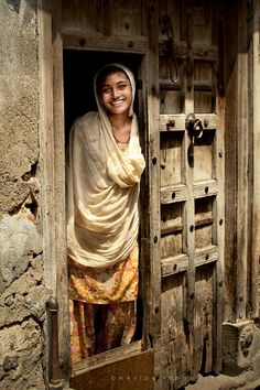 a woman standing in an open doorway with a shawl on her head and smiling at the camera